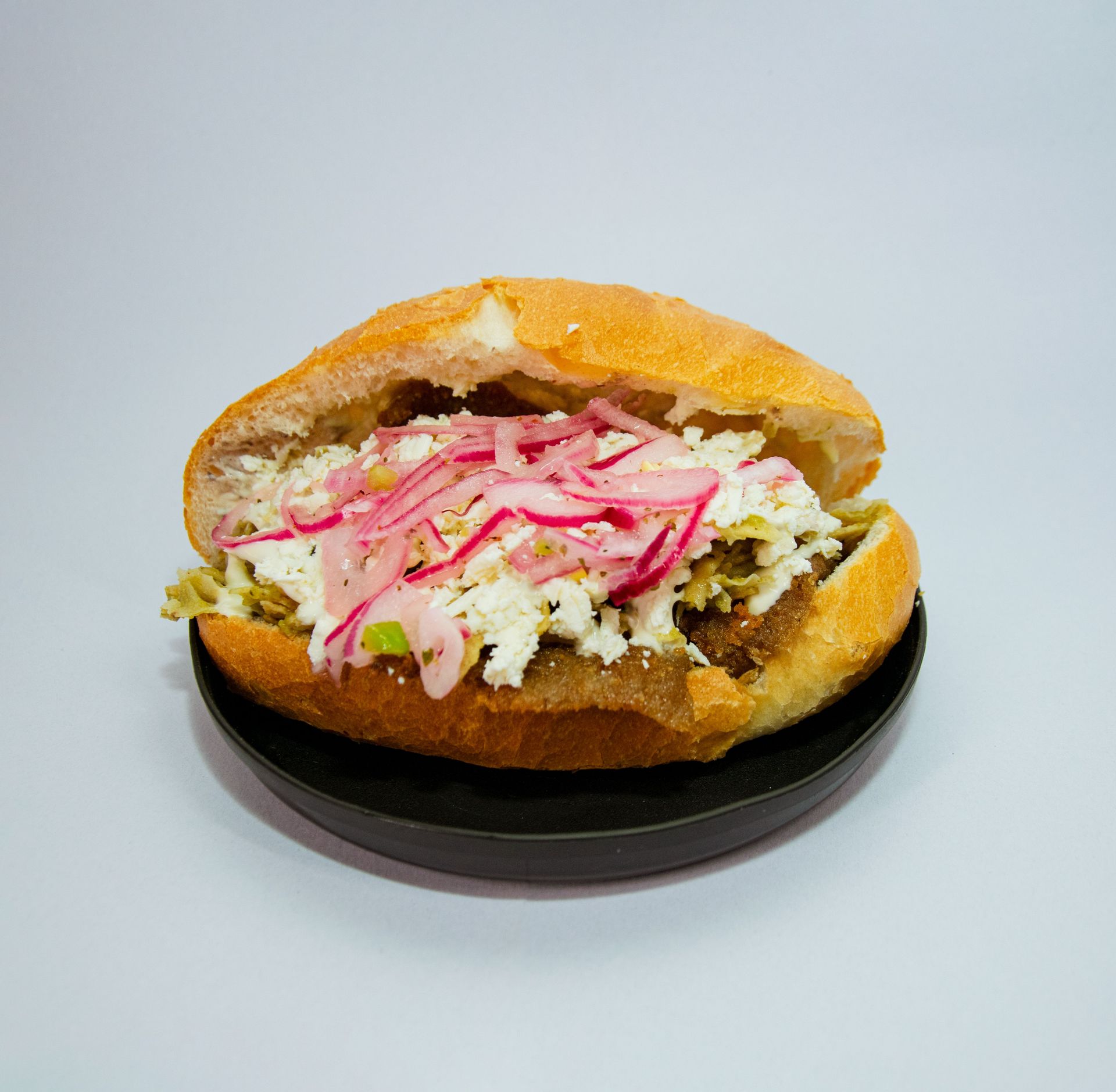 A delicious Mexican torta topped with pickled onions and cheese on a black plate.