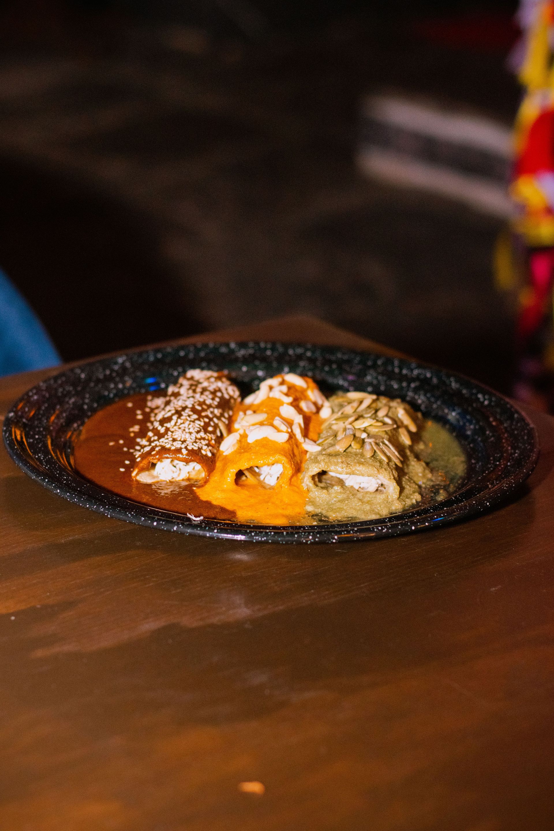 Close-up of Mexican enchiladas with vibrant sauces photographed indoors with warm lighting.