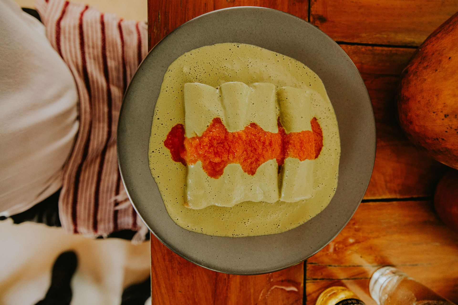 Top-down view of enchiladas with green sauce and red salsa on a rustic wooden table.