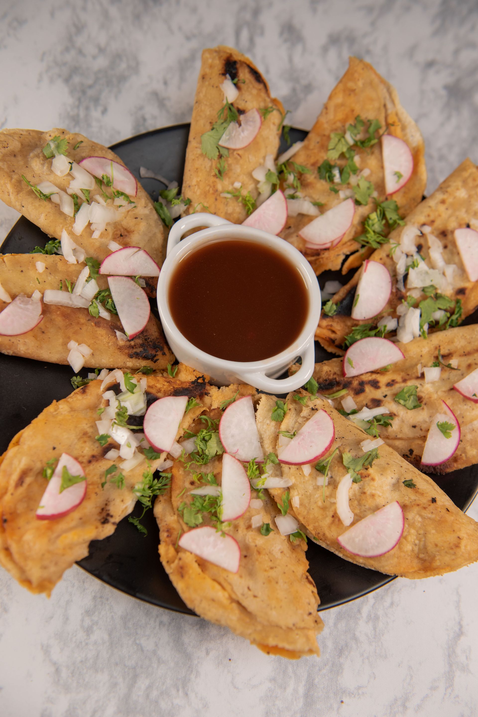 A plate of Mexican tacos garnished with radishes and served with a rich dipping sauce.
