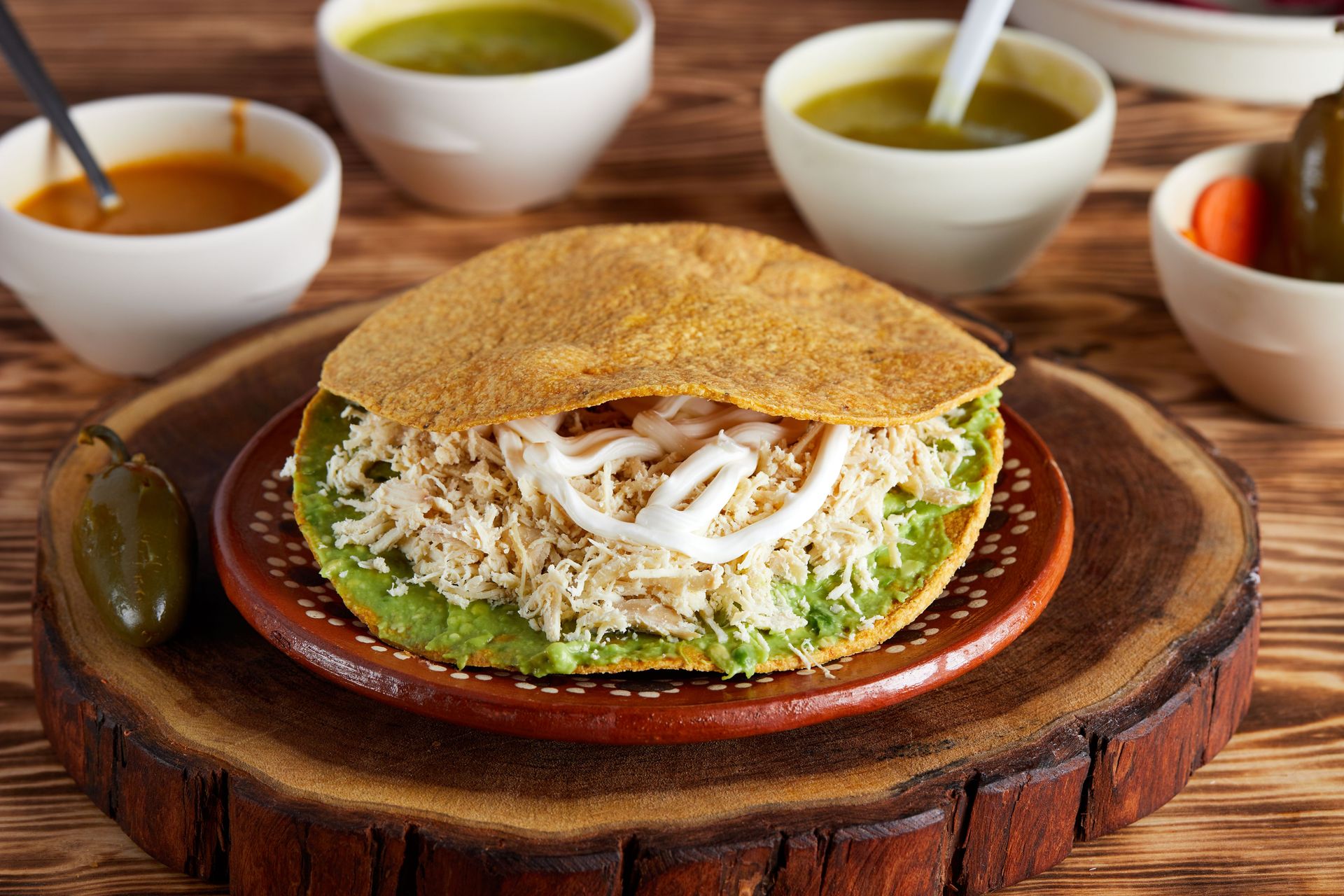 Delicious Mexican tostada topped with chicken and avocado served with colorful sauces.